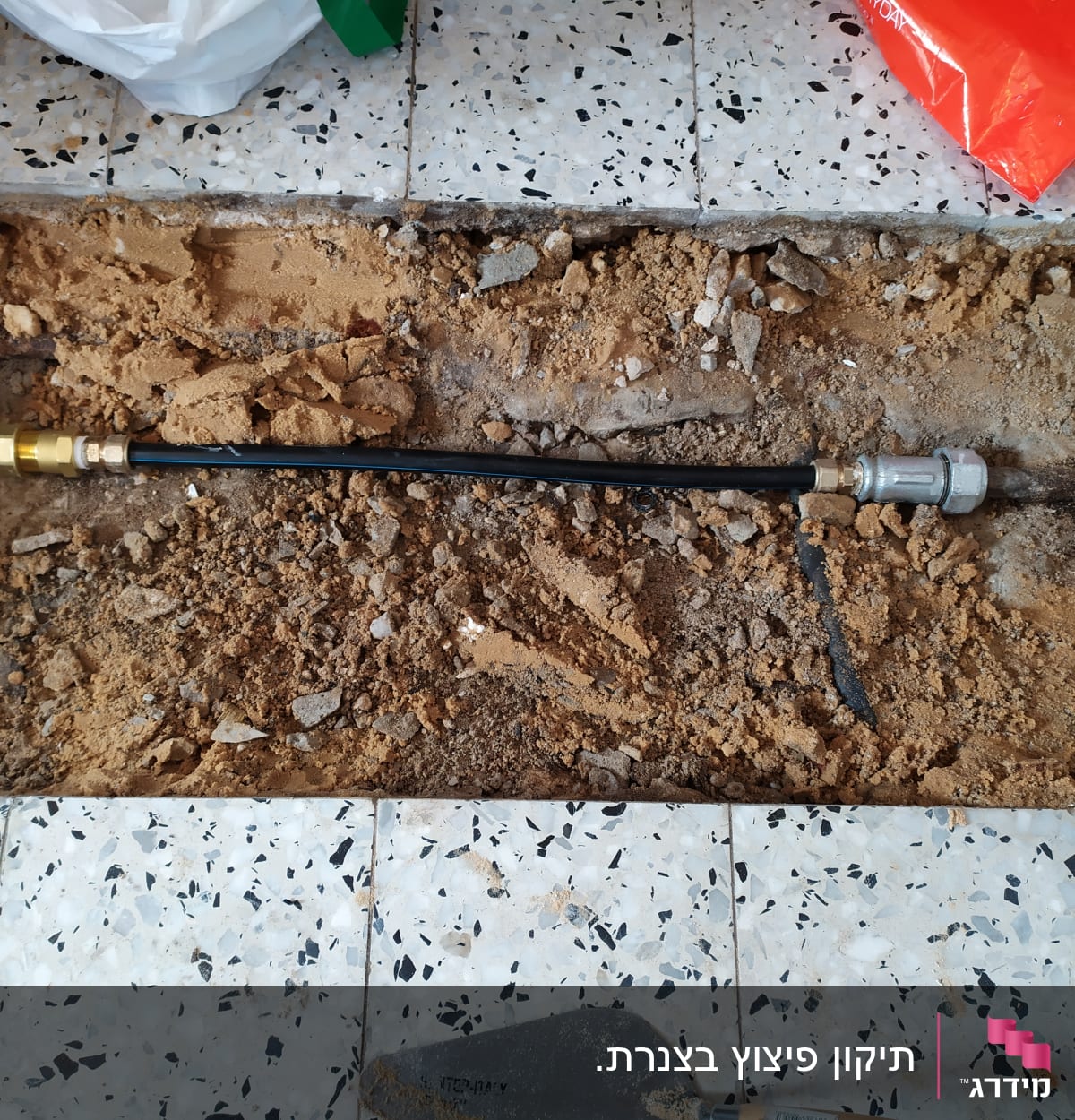 צינור שחור עם מחברים מתכתיים בתוך חפירה ברצפה